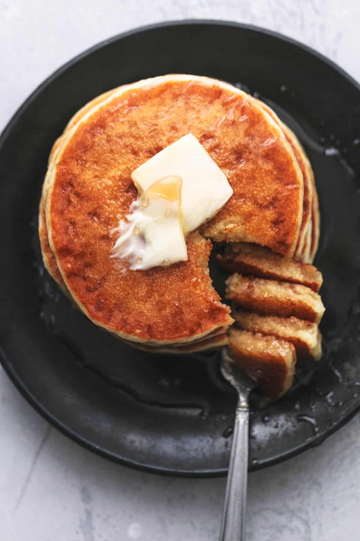 Beißen Sie aus einem Stapel Pfannkuchen auf einem Teller mit Butter und Sirup