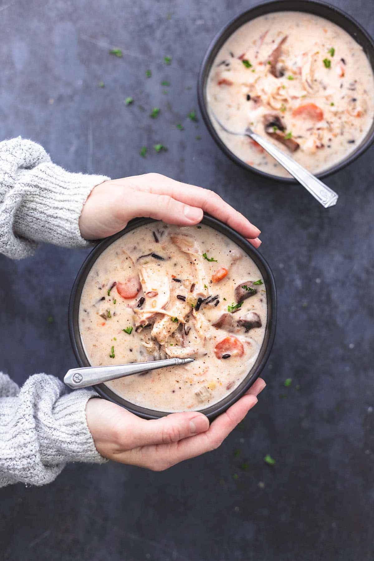 Hände halten schwarze Suppenschüssel mit Hühnchen-Wildreissuppe