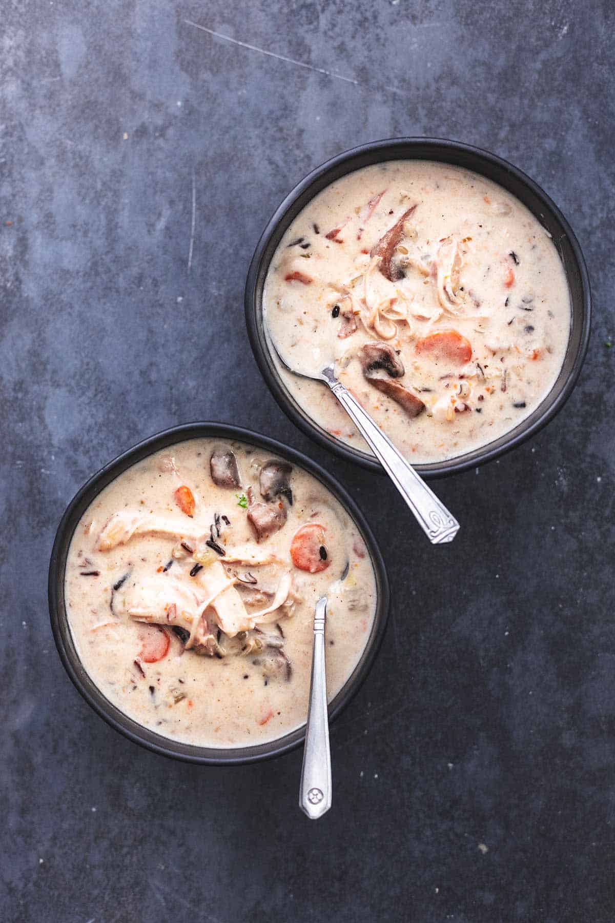 zwei schwarze Schalen mit Hühnchen-Wildreis-Suppe mit Löffeln