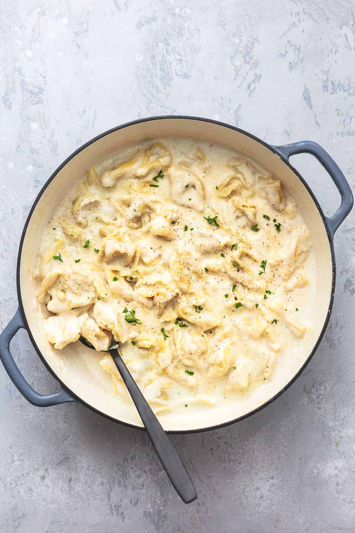 Tortellini mit Alfredo-Sauce in einer Pfanne mit einem Servierlöffel